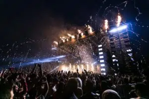 A crowd of people at an entertainment event with music and fireworks in the background.